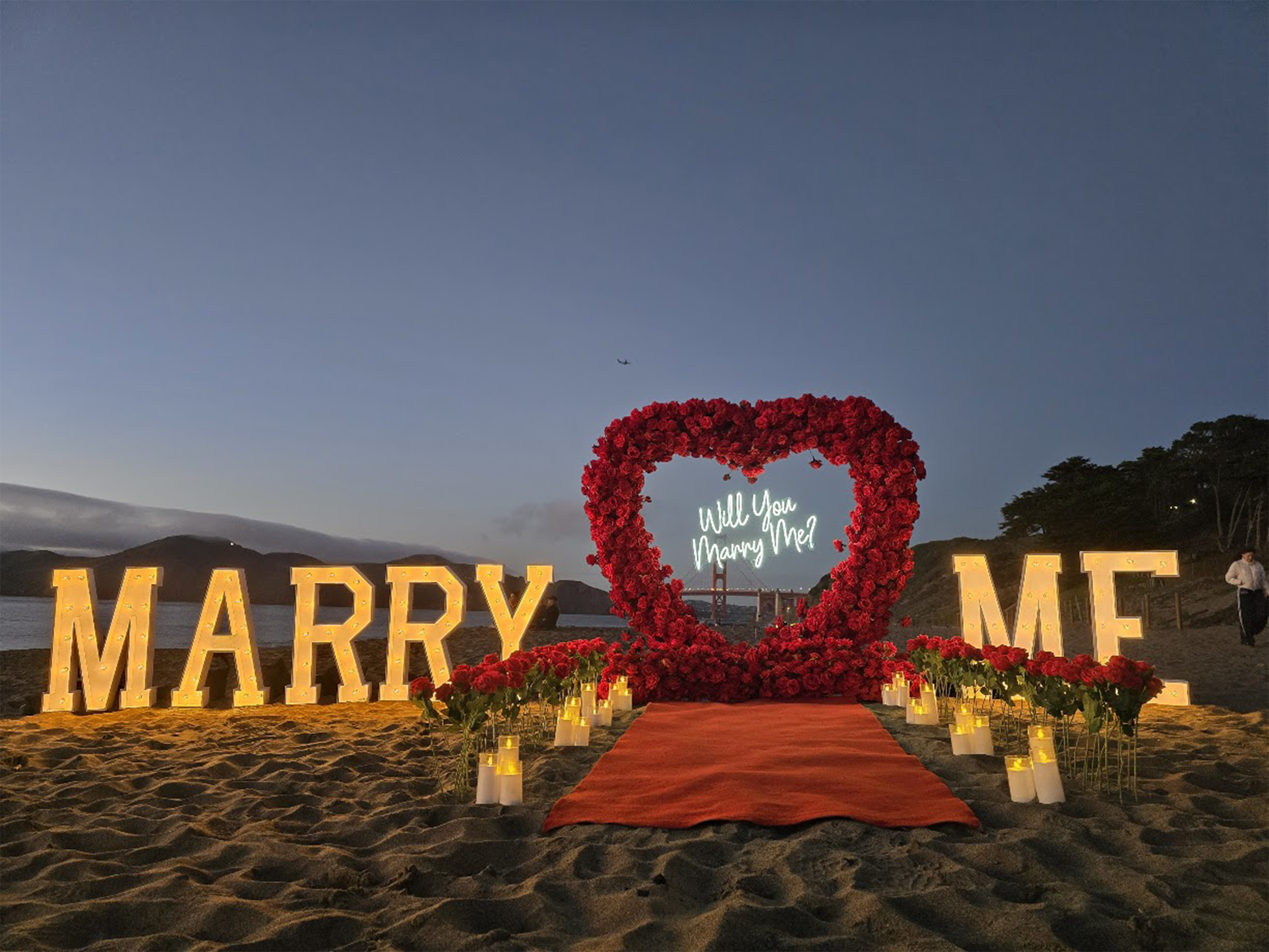 San Francisco Bay Area Baker Beach proposal with red heart arch, warm marquee letters and candles