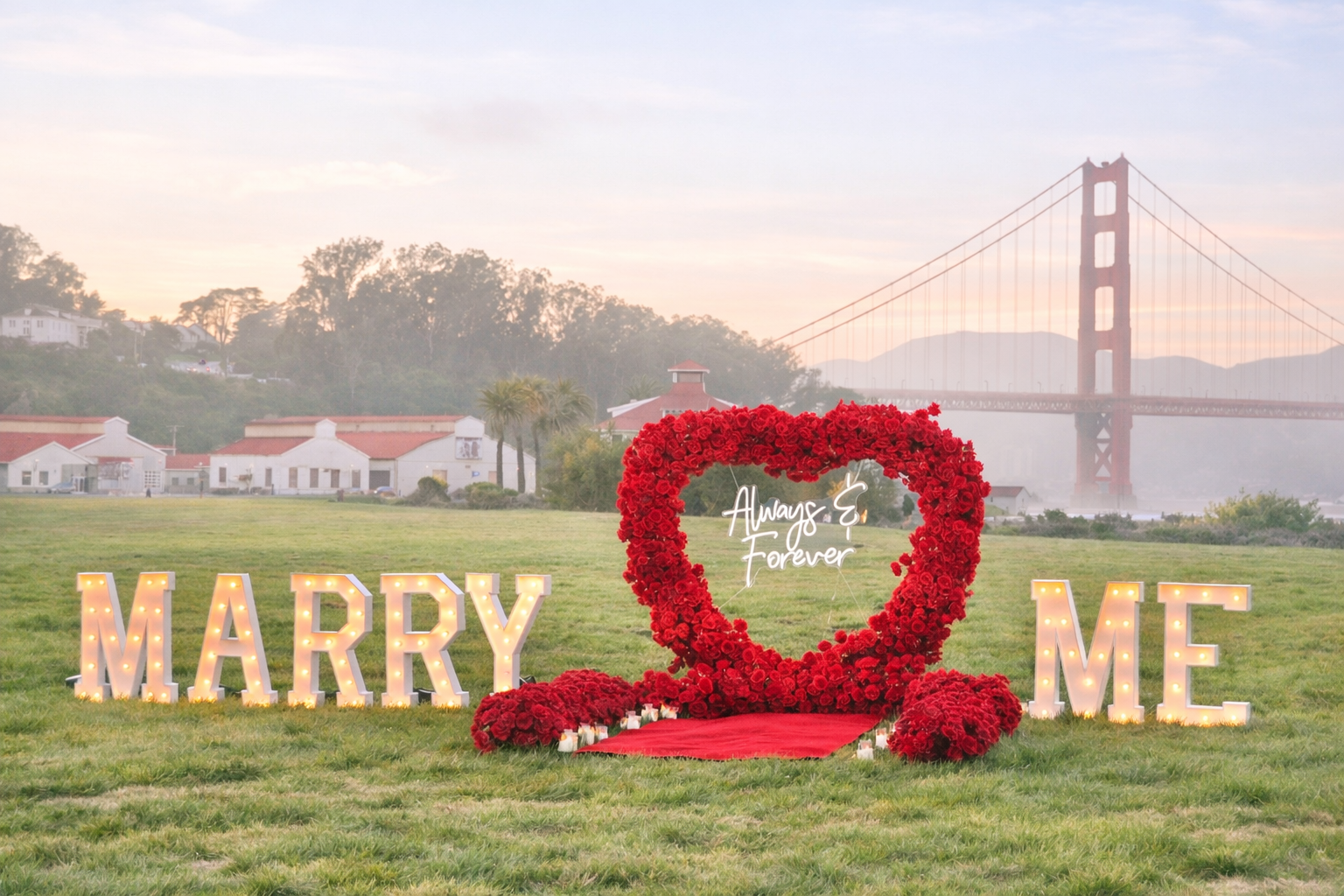 Marquee MARRY ME letters with red heart arch proposal setup at Crissy Field, San Francisco with Golden Gate Bridge view