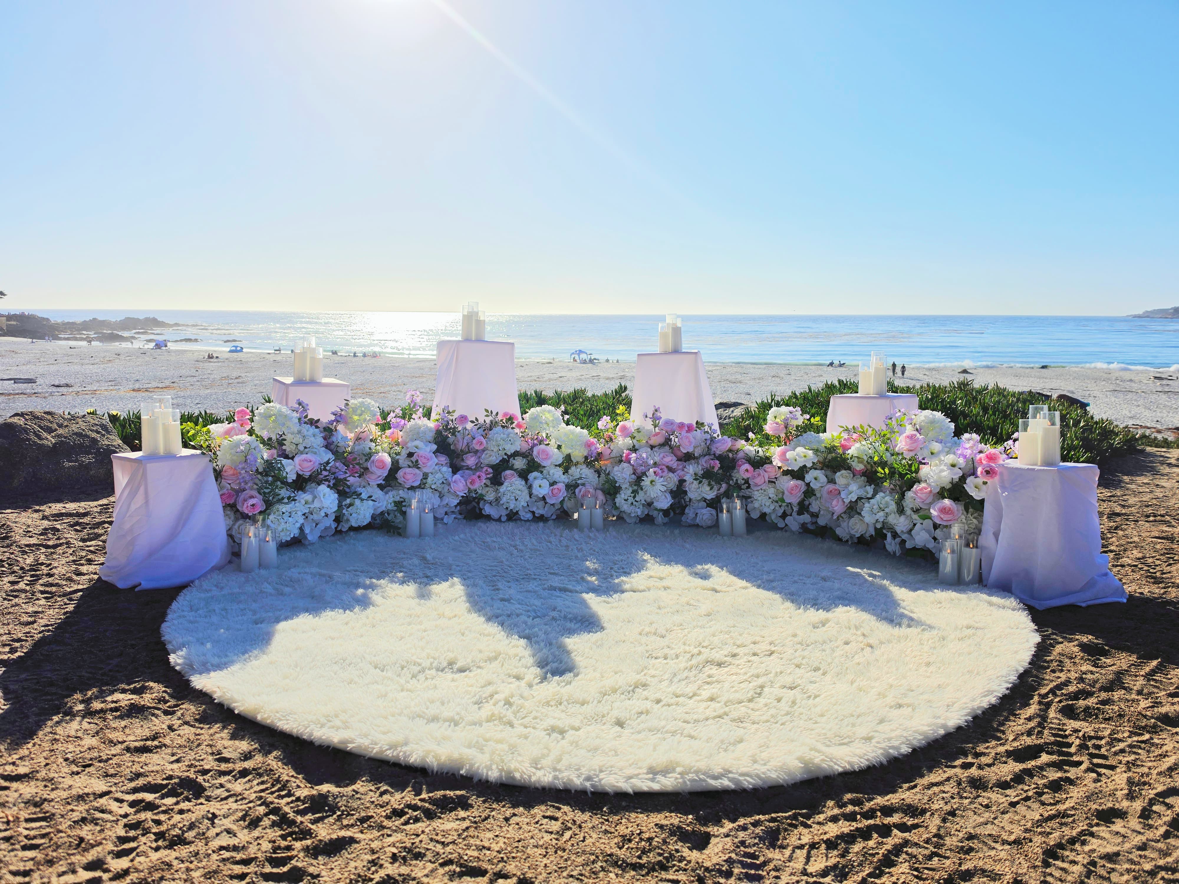 The Enchanted Romance – blush pink, white, and lavender grounded florals with candlelit white pedestals and a fluffy white rug overlooking the water at Carmel Beach