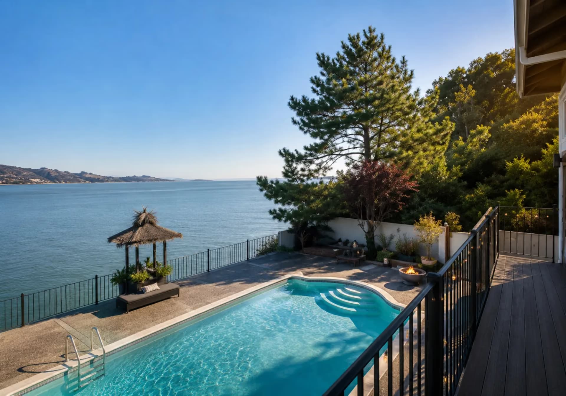 Private waterfront pool deck at ERIA Corte Madera with a thatched-roof gazebo overlooking Corte Madera Bay and the Marin hills