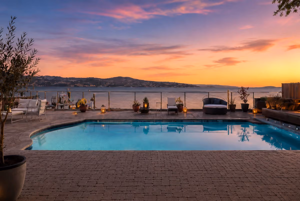 ERIA Corte Madera pool and hot tub glowing at sunset with lantern-lit poolside seating and bay views