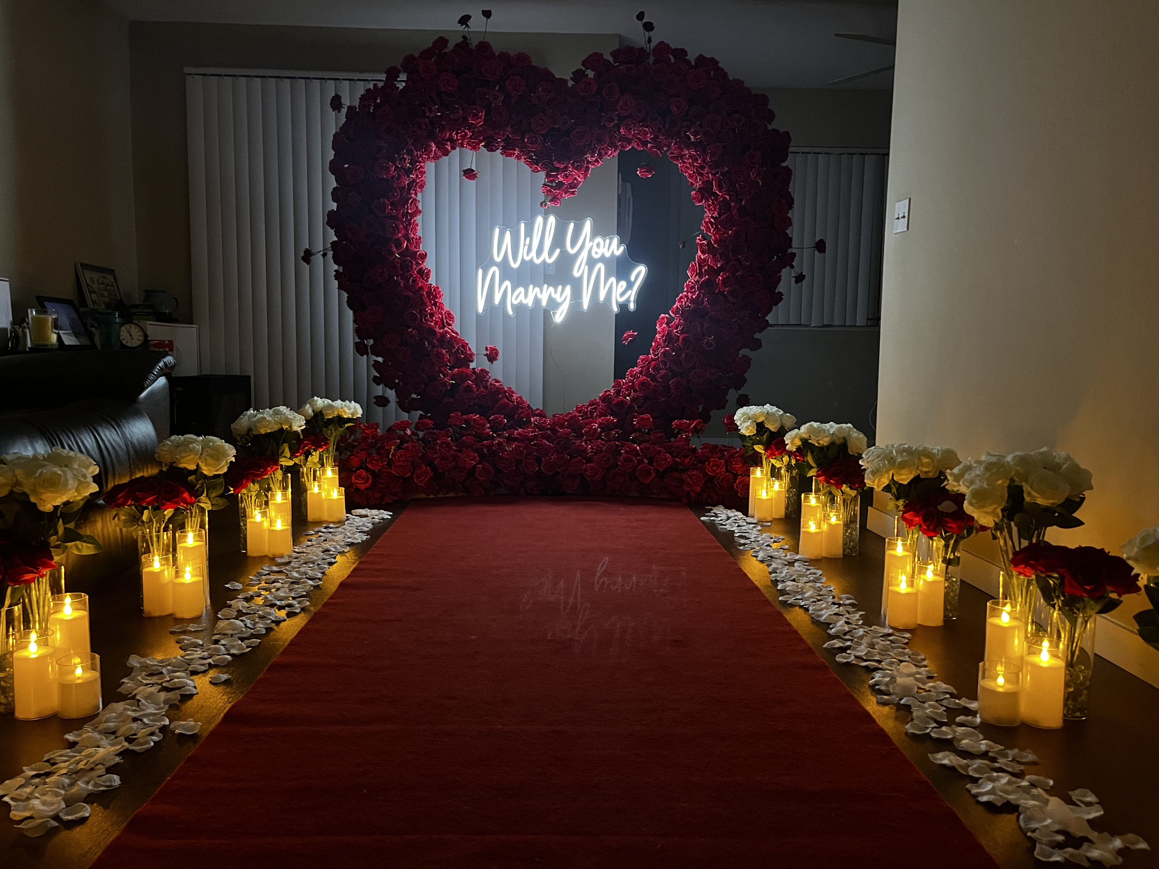 Indoor bay area proposal setup with red arch and white flowers in vases