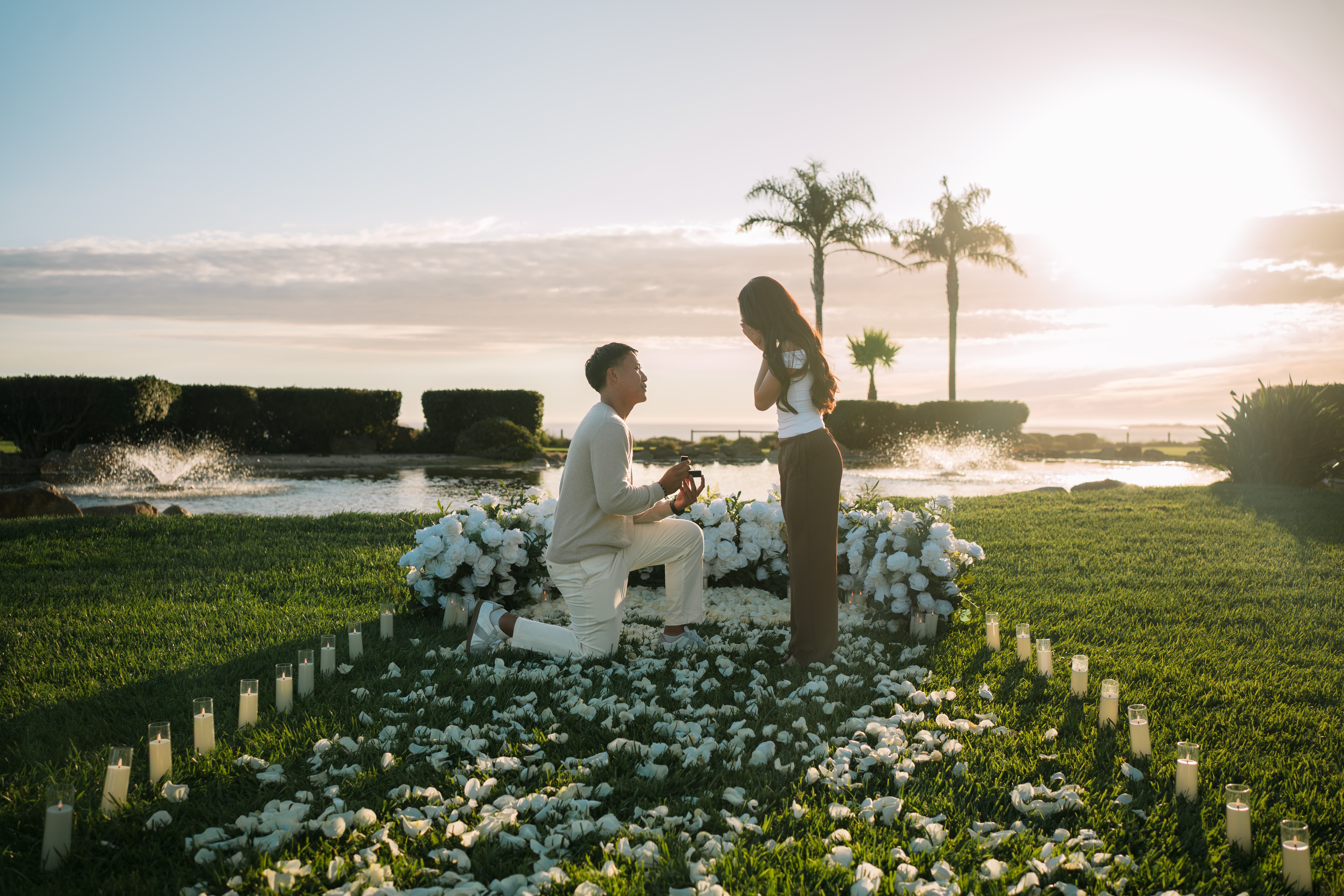 The Intimate Promise Package at sunset on the Island lawn at Seascape Beach Resort, with a white rose ground arrangement, a dense white petal bed and scattered petal walkway, and pillar candles beside the koi pond